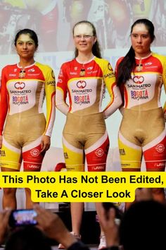 Three women in tight cycling uniforms on a stage with an audience taking photos
