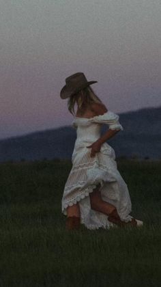 Woman in a white dress and cowboy hat in a field at dusk