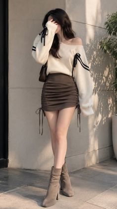 Woman in an off-shoulder sweater and ruched skirt with ankle boots outdoors