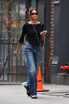 Woman in sunglasses and jeans walking on a city street with earbuds