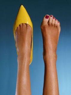 One foot in a yellow high heel and one bare foot with red nail polish