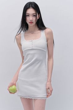 Woman with long black hair in a white tank top dress holding a green apple