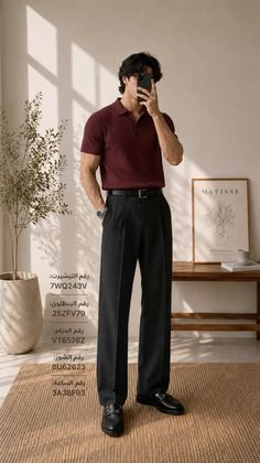 Man in a maroon polo shirt and black pants taking a mirror selfie indoors