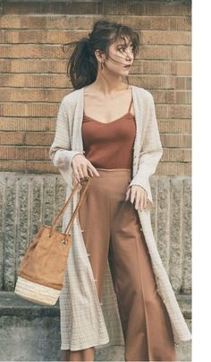 Woman in a long cardigan and brown camisole holding a bucket bag outdoors