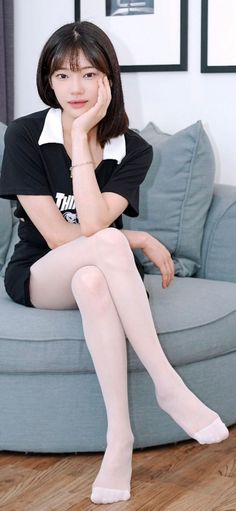 Woman with short black hair wearing a black shirt and white tights, sitting on a couch