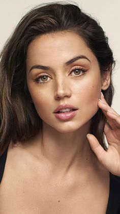 Woman with long brown hair and pink lips, touching her cheek