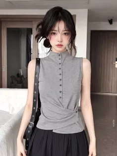Woman with black hair wearing a gray sleeveless top and black pleated skirt indoors