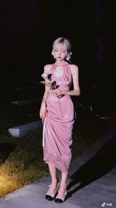 Woman in a pink halter neck dress holding a rose at night
