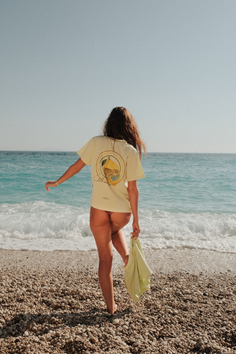 Woman in a t-shirt and bikini bottoms on a pebble beach facing the ocean