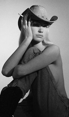 Woman in a cowboy hat and jeans, with exposed skin, holding a cigarette