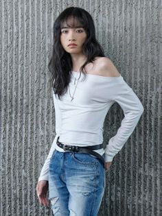 Person with long dark hair wearing an off-shoulder top and ripped jeans indoors