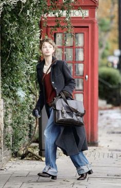 Woman in a long coat and jeans walking past a red telephone booth