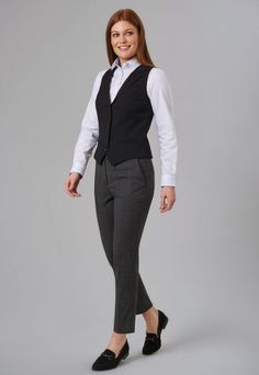 Woman in a black vest and grey pants smiling in a studio shot