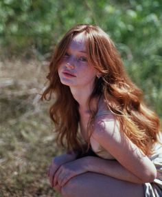 Woman with long red hair and freckles crouching outdoors