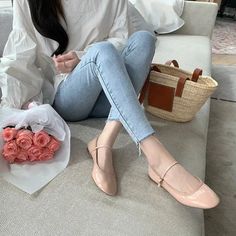 Woman in a white blouse and blue jeans sitting with a bouquet of pink roses