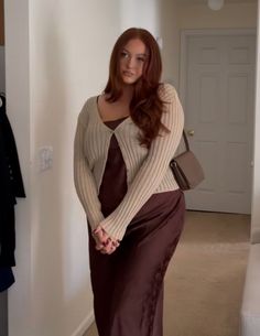 Woman with long red hair wearing a brown slip dress and cardigan indoors