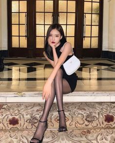 Woman in a black dress and pantyhose sitting indoors with a white handbag