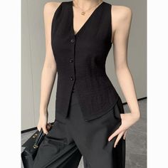 Woman in a black vest and pants holding a black handbag