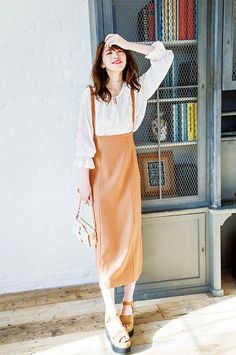 Woman in a brown overall dress and white blouse posing indoors