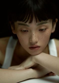 Person with short hair and freckles wearing a white tank top, looking down