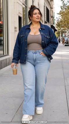 Woman in a denim jacket and jeans walking on a city street with iced coffee