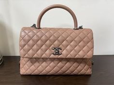 Pink quilted leather top handle bag with a silver logo on a dark surface