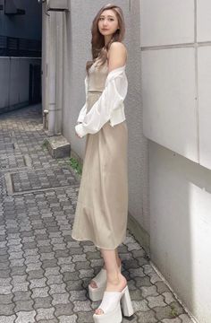 Woman in a beige dress and white shirt standing on a paved street