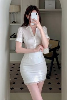 Woman in a white shirt and mini skirt taking a mirror selfie indoors