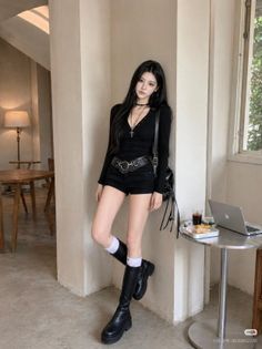 Woman with long black hair wearing a black top, shorts, and knee-high boots indoors