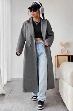 Woman in a long gray coat, crop top, and baggy jeans indoors