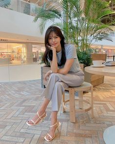 Woman with long hair sitting indoors in a light blue top and heeled sandals