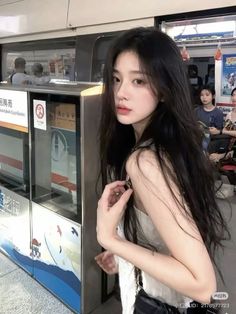 Woman with long black hair in a white top at a subway station