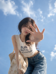 Woman in a crop top and jeans posing against a blue sky with clouds