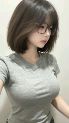 Woman with short hair and glasses wearing a tight grey t-shirt indoors