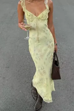 Woman in a yellow floral dress and cowboy boots holding a wine glass