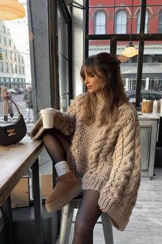 Woman in a chunky knit sweater and black tights sitting at a cafe window