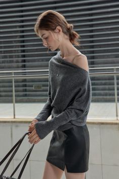 Woman in an off-shoulder gray sweater and black leather skirt outdoors
