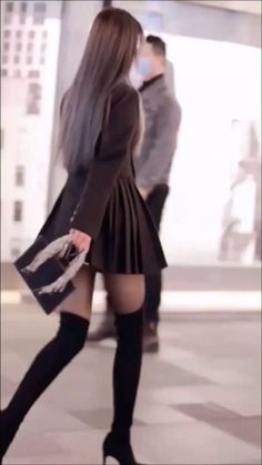 Woman with long hair in a black pleated skirt and thigh high boots walking on a street