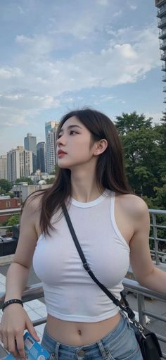 Woman in a white tank top and jeans on a city rooftop looking into the distance