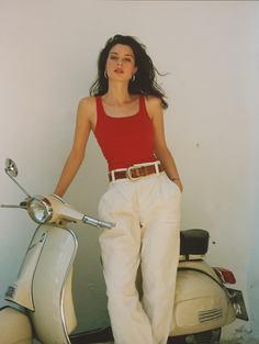 Woman in a red tank top and white pants posing with a scooter outdoors