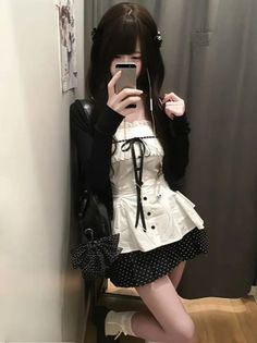 Woman in a maid-style dress and black cardigan taking a selfie indoors