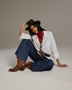 Woman in a cowboy hat, red scarf, and wide leg jeans sitting on a studio floor