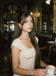Woman with long hair and heart earrings in a cafe, holding a cup of coffee