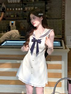 Woman in a white sailor dress with a navy bow indoors
