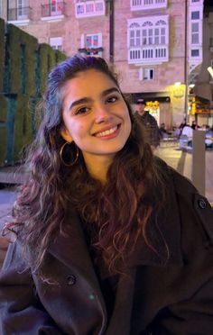 Smiling woman with long curly hair and hoop earrings outdoors at night