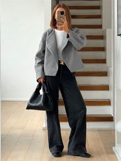 Woman in a gray jacket and wide leg pants taking a mirror selfie indoors
