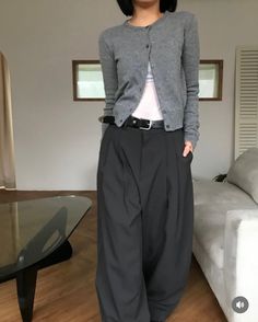 Person in a gray cardigan and wide leg pants standing indoors