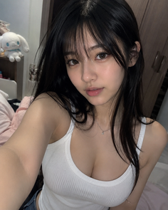 Woman with long black hair wearing a white tank top indoors