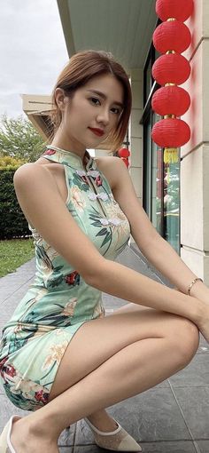 Woman in a floral cheongsam squatting outdoors with red lanterns