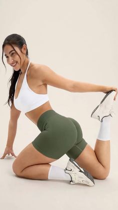 Woman in a white sports bra and olive athletic shorts posing in a studio